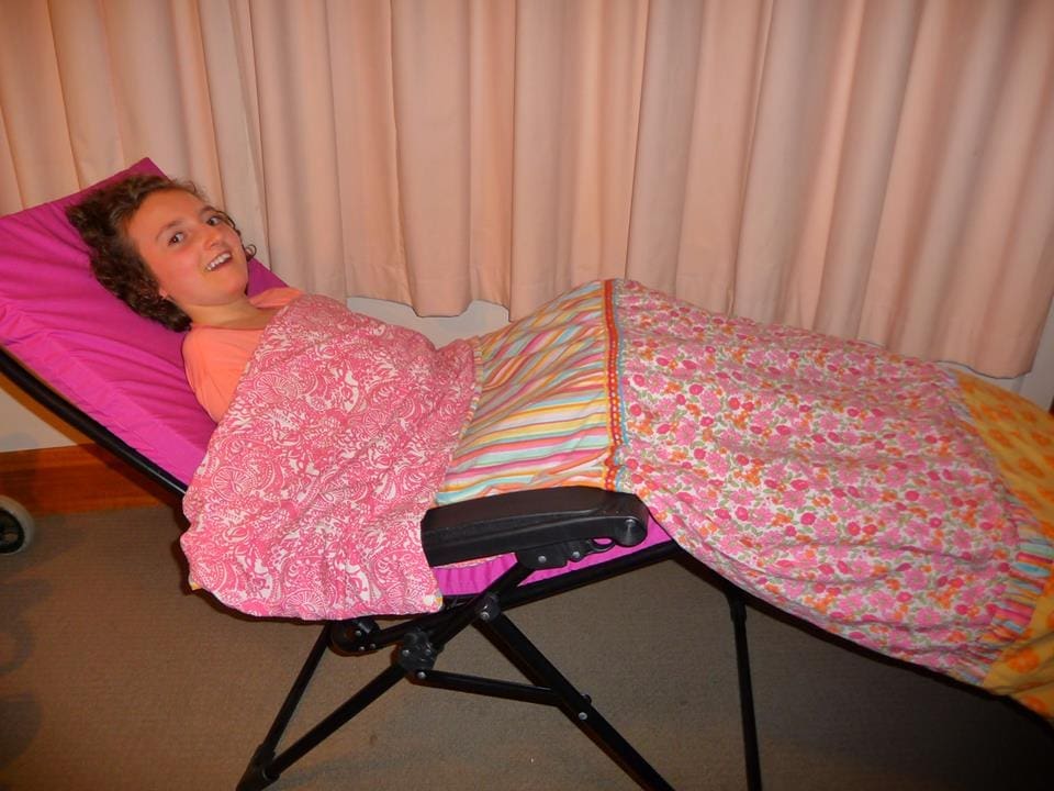 A girl rests on a pink camping chair adapted as a travel bed with a striped blanket.