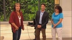 Three people stand in front of a backdrop of greenery, with a camera on a tripod between two of them.