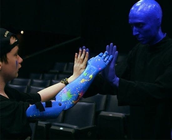 A Blue Man Group performer high-fives a person wearing a blue robotic arm.