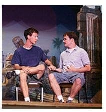 Two men sit on chairs facing each other with their hands clasped.