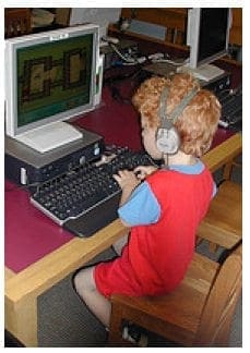Child with headphones works on a computer at a desk.
