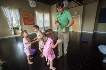 A man in a green shirt leads three young children in a movement activity.