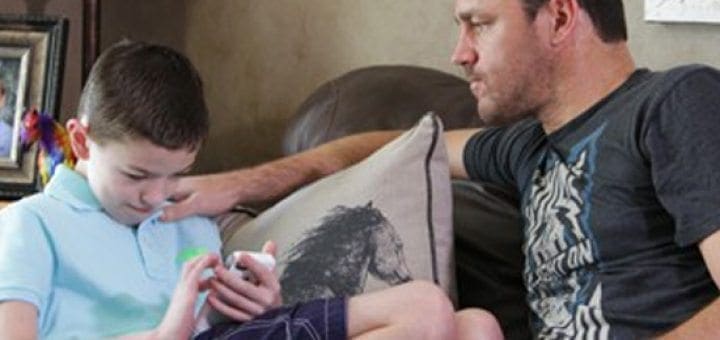 Man and boy on a couch with the boy looking at a phone.
