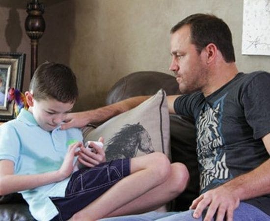 Man and boy on a couch with the boy looking at a phone.