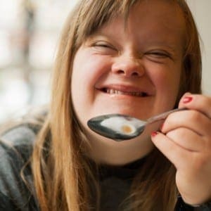 Young woman with Down syndrome eating from a spoon.