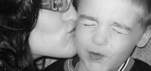Mother kissing her child on the cheek in a black and white close-up.