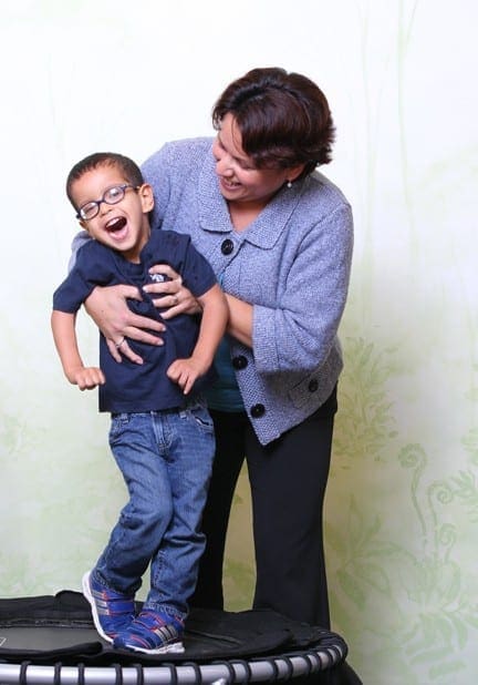Woman holding a laughing boy wearing glasses while standing on a trampoline.