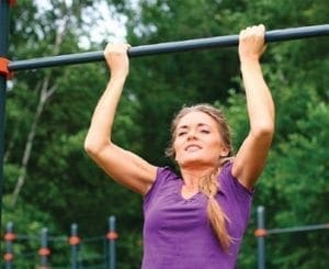 Woman performing a pull-up on monkey bars at a playground.