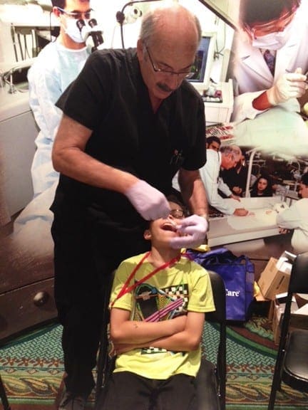 Dentist demonstrating proper tooth brushing technique on a child in a chair.