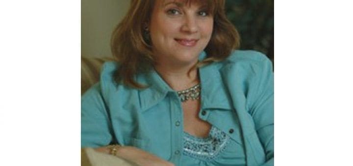 Woman in a teal shirt smiles while resting her hands on a pillow.