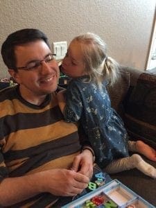 Child kissing her father on the cheek while they play with alphabet letters.