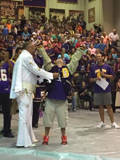Special Olympian receives a letter jacket from an Elvis impersonator at a pep rally.