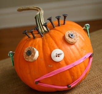 Pumpkin decorated with screws, corks, buttons, and pink ribbon to resemble a face.