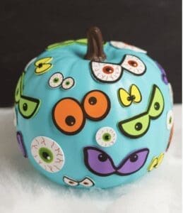 Light blue pumpkin decorated with various googly eyes and monster eyes.