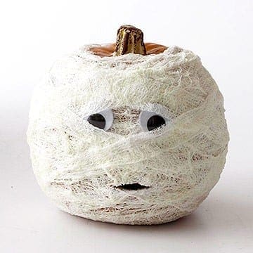 A pumpkin covered in white gauze strips with googly eyes and a black mouth to resemble a mummy.