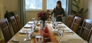 Woman in polka-dot dress setting a formal Thanksgiving table.
