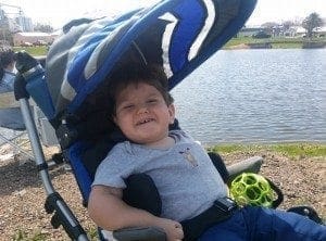 Child in a stroller by a lake smiling.