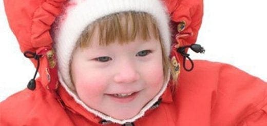 Child in a red winter coat and white hat smiling
