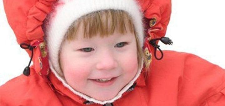 Child in a red winter coat and white hat smiling