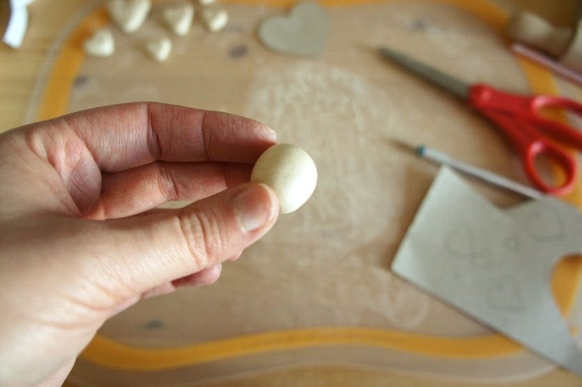A hand holds a small ball of beige clay.