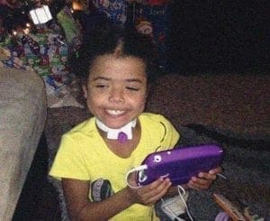 Child wearing a neck brace and yellow shirt holds a purple electronic device.