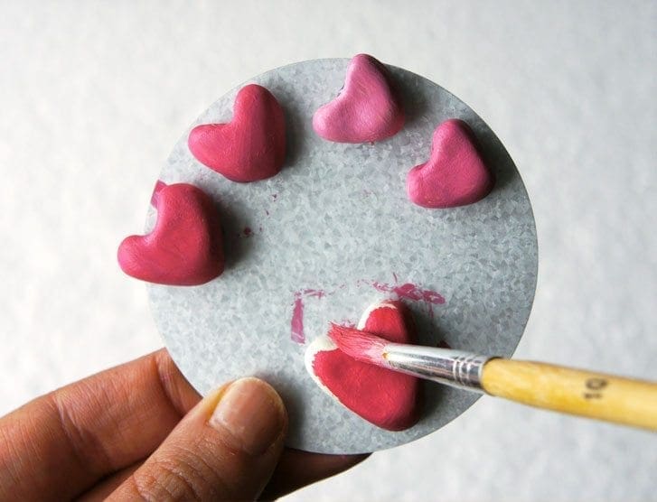 Hand painting small pink clay hearts arranged on a circular gray surface.