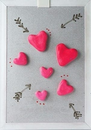 Several pink heart-shaped magnets are arranged on a gray surface with drawn arrows.