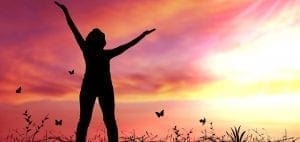 Silhouette of a person with arms raised against a colorful sunset and butterflies.