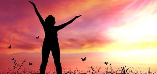 Silhouette of a person with arms raised against a colorful sunset and butterflies.