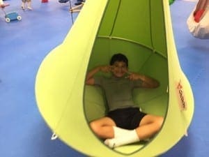 Child sits in a green pod swing making a funny face.