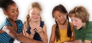 Four children gather around a table, looking at something small in their hands.