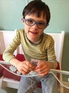 Young boy wearing glasses and a striped shirt sits on a bench holding a small card.