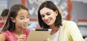 A teacher and a young girl look at a tablet together in a classroom.