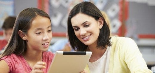 A teacher and a young girl look at a tablet together in a classroom.
