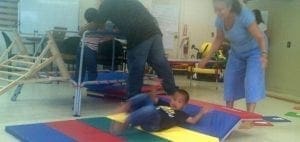 A young boy lies on a colorful mat while adults stand nearby.