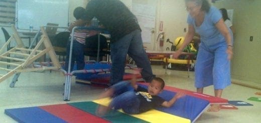 A young boy lies on a colorful mat while adults stand nearby.