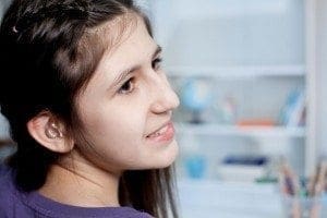 A young person with a hearing aid smiles while looking to the right.