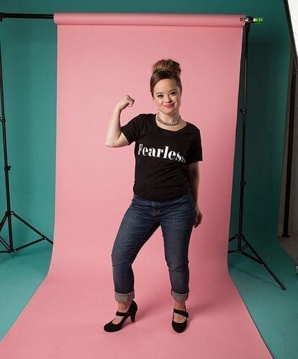 Katie Meade poses with her arm flexed in a "fearless" shirt and jeans.