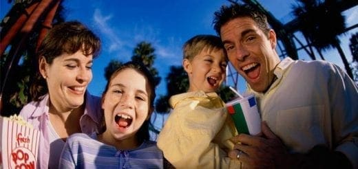 A family laughs and cheers while holding popcorn and drinks.