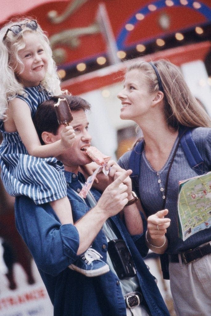 Family with daughter on shoulders at an outdoor event.