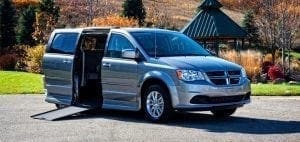 Silver accessible van with side door open and ramp extended.