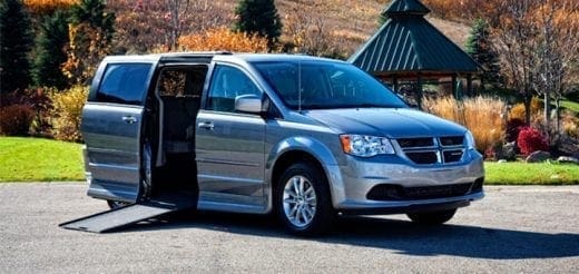 Silver accessible van with side door open and ramp extended.