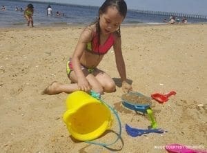 Young girl plays with sand toys on a sunny beach with the ocean in the background.