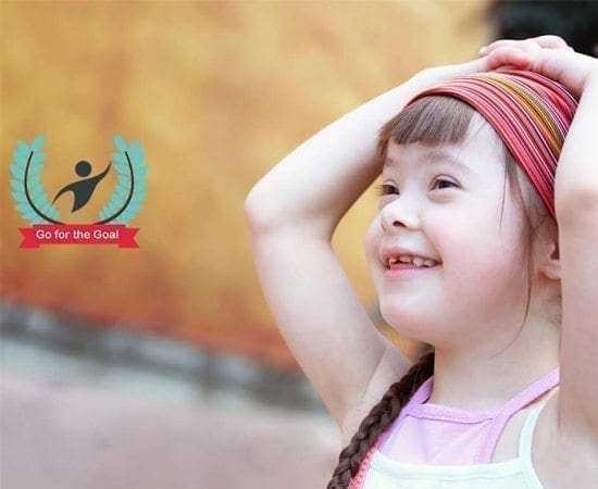A young girl with a braid smiles with her hands behind her head next to a logo that says "Go for the Goal.