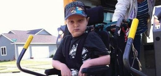 A boy wearing a baseball cap and t-shirt sits in a wheelchair.