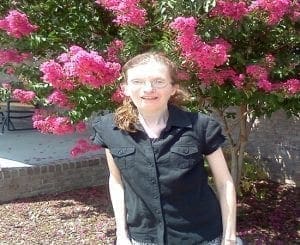 Jenni Anderson smiles in front of a flowering tree.