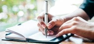 Hands writing in a journal with a pen