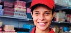A woman wearing a red cap smiles in front of shelves of products.