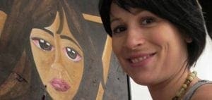 Woman smiles next to a painting of a person with large eyes.