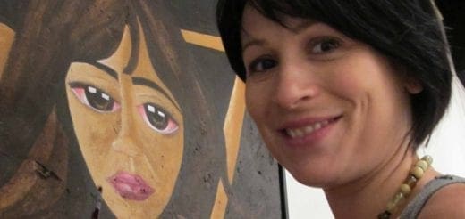 Woman smiles next to a painting of a person with large eyes.